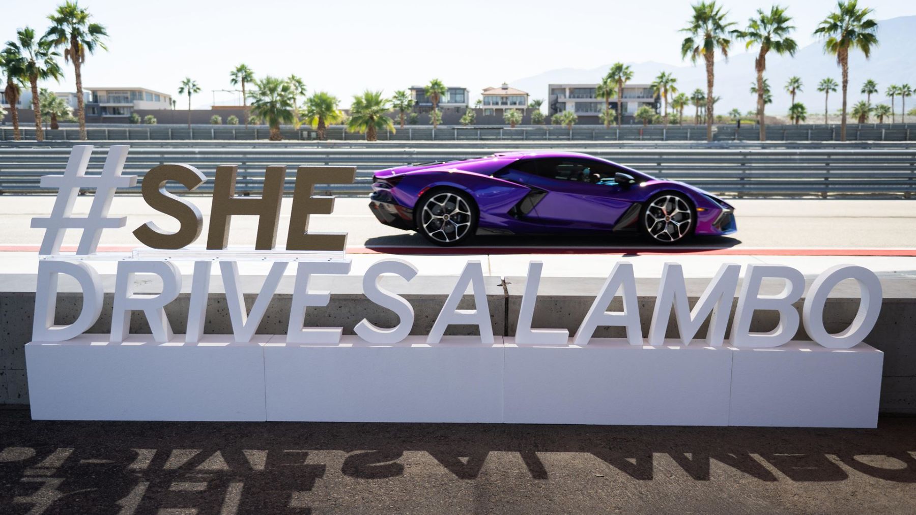 #SheDrivesALambo sign trackside with a purple Lamborghini Revuelto