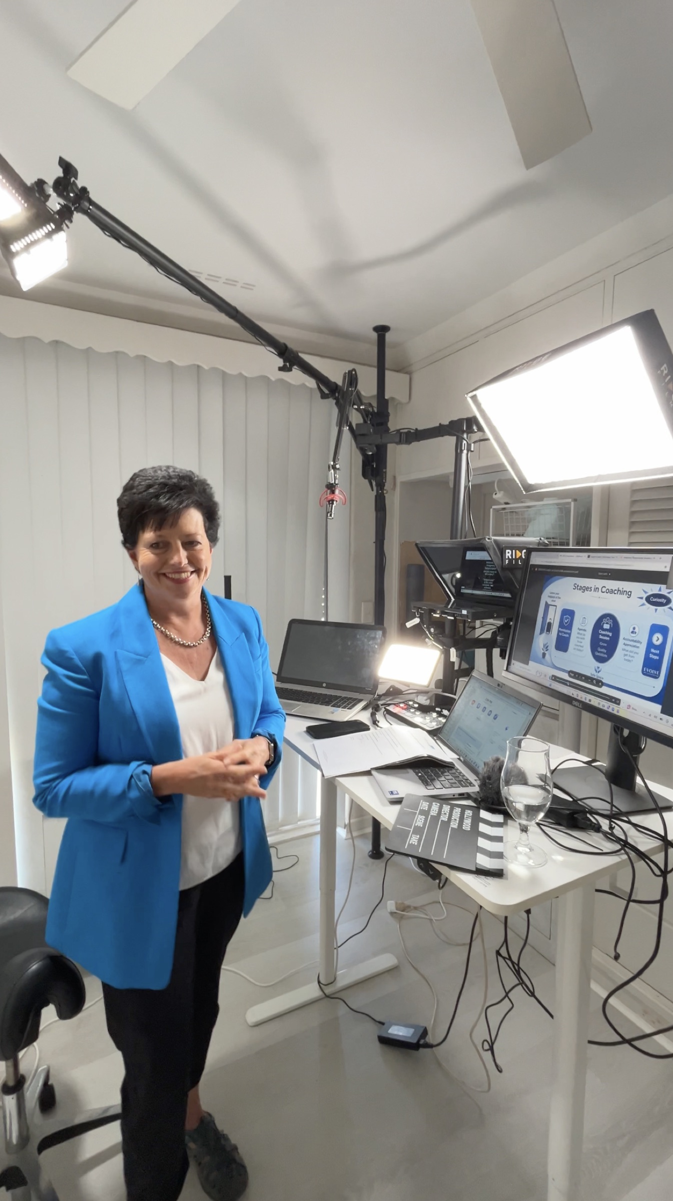 A client smiling beside her studio setup, with a coaching lesson loaded on the teleprompter