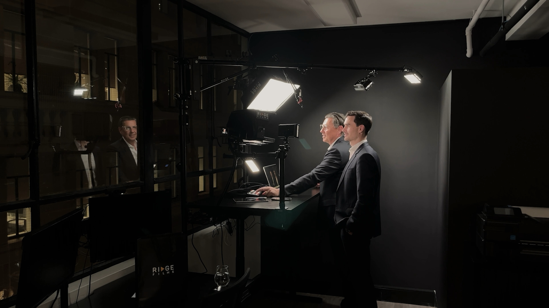 Two men in suits recording in a dark corporate office