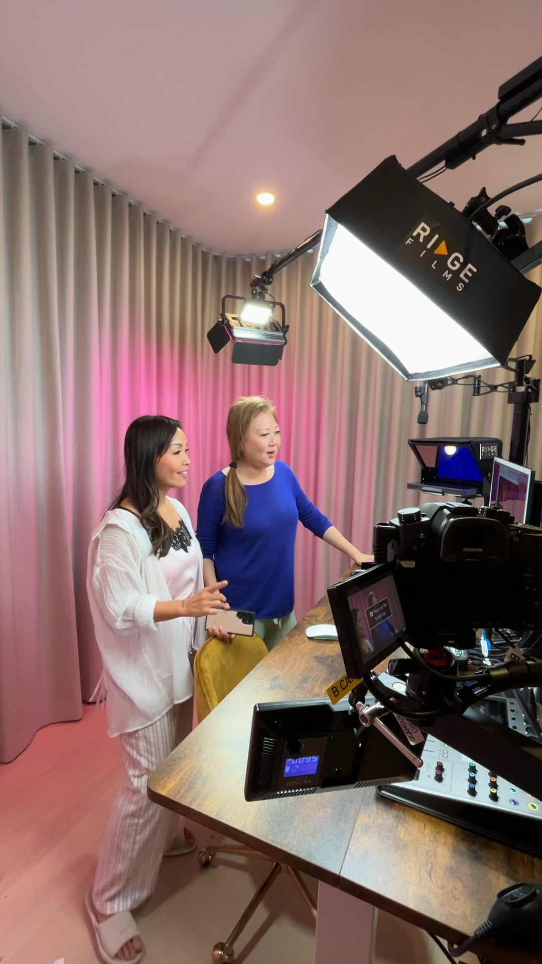 Two women presenting in a pink-lit studio room