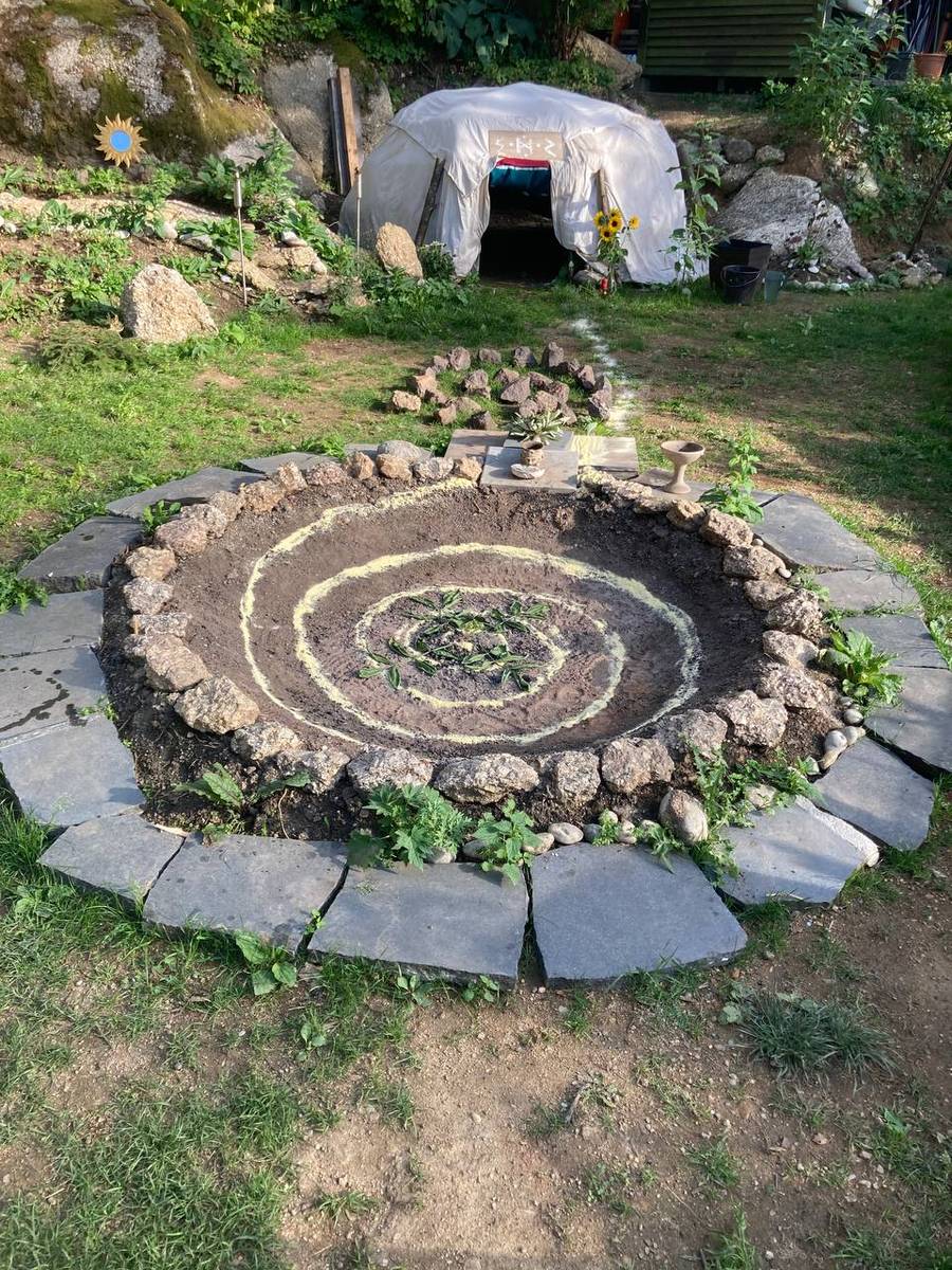 Steinspirale im Garten, dahinter die Schwitzhütte