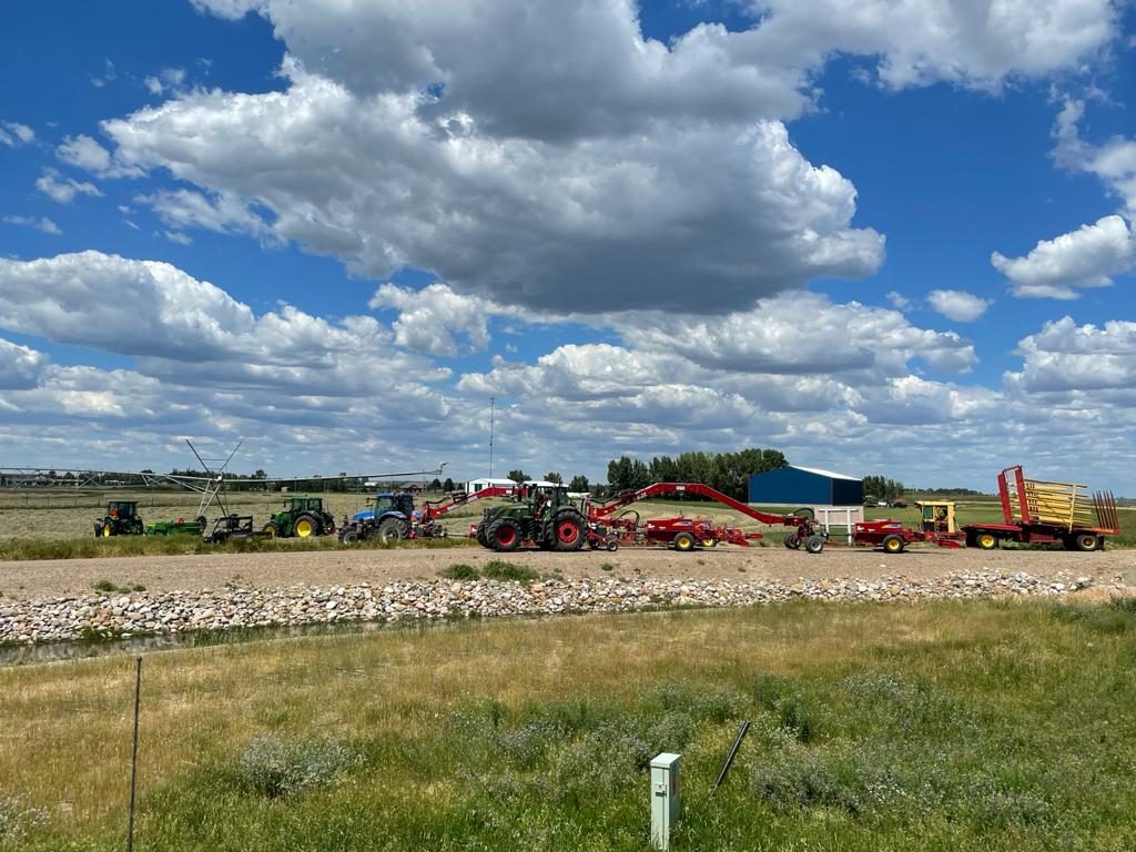 Hay-handling equipment lined up near an irrigated field.