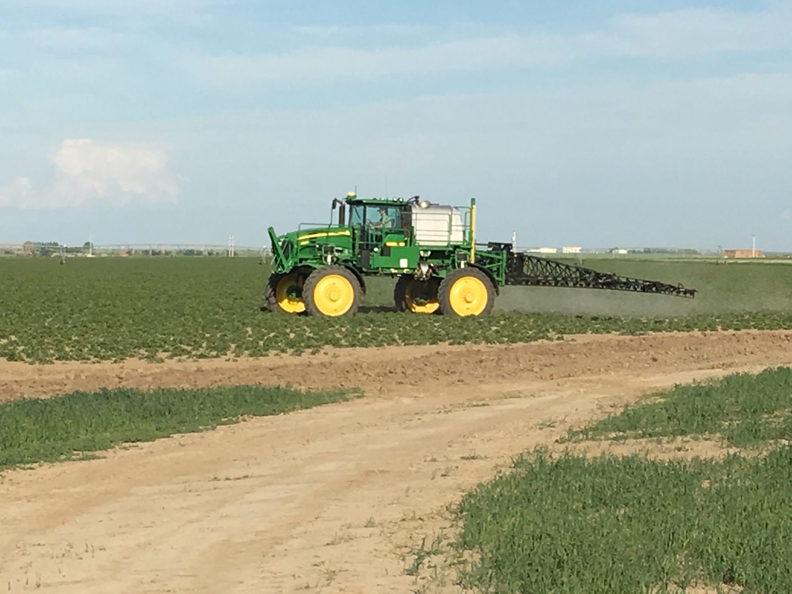 A John Deere self-propelled sprayer working across a green crop field.