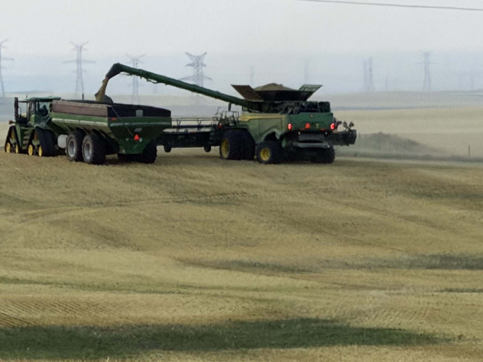 A John Deere combine transfers grain to a cart during harvest.