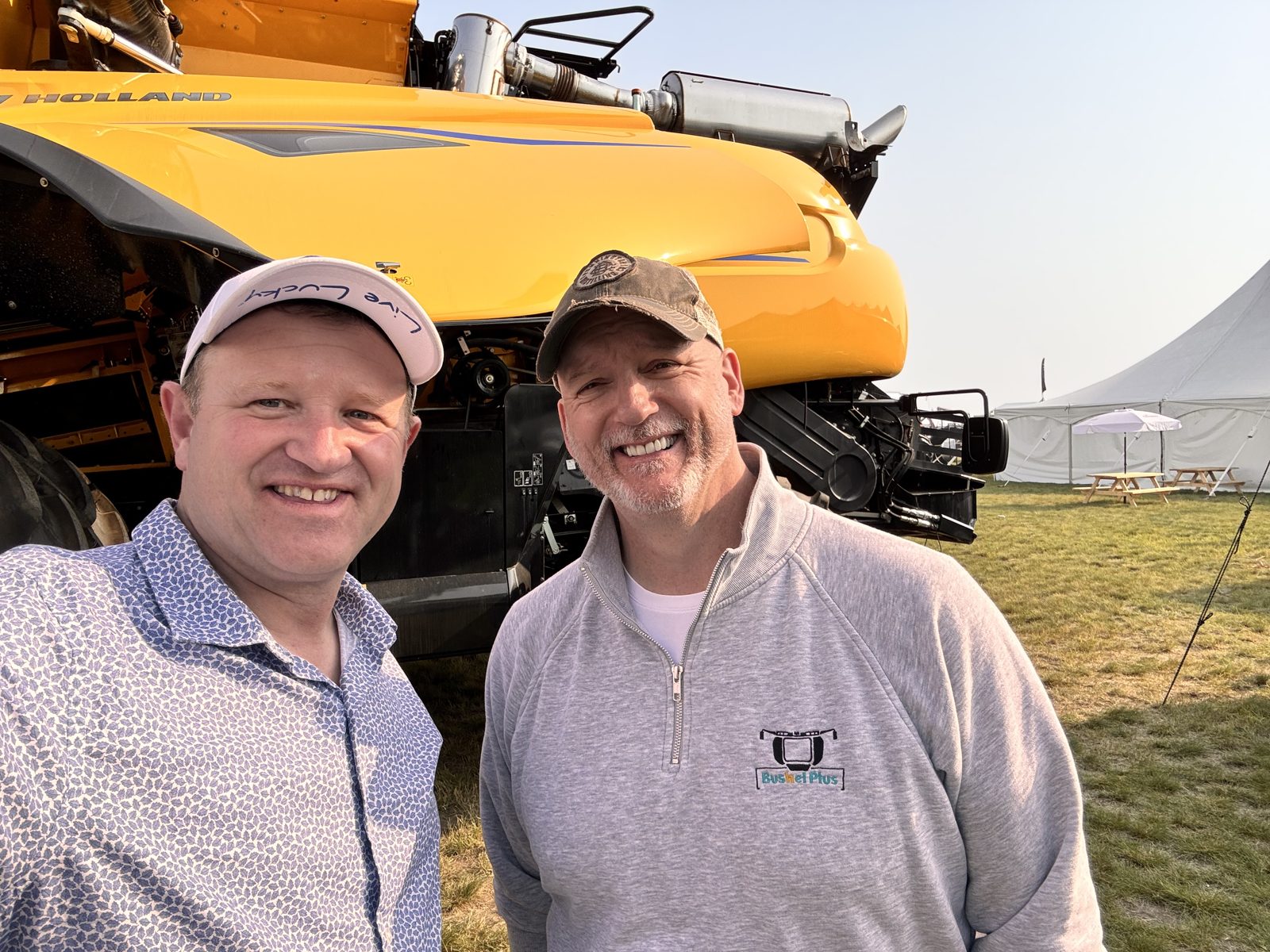 A moment beside a New Holland combine, with Bushel Plus represented.
