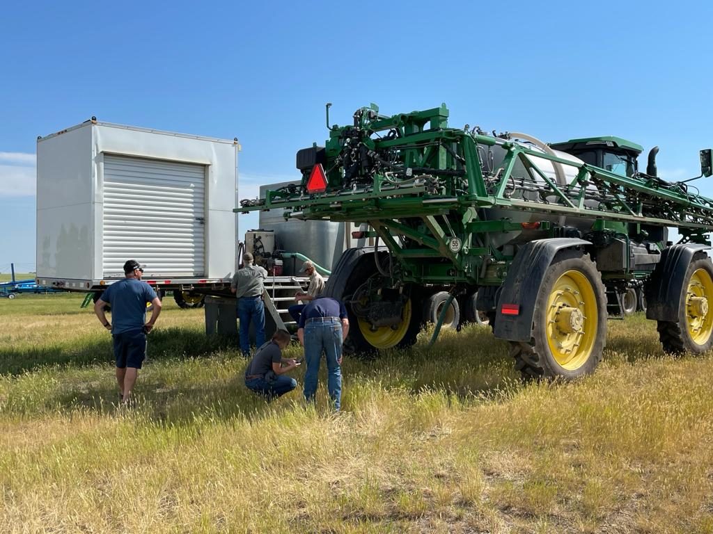 A John Deere sprayer beside a tender truck during field operations.