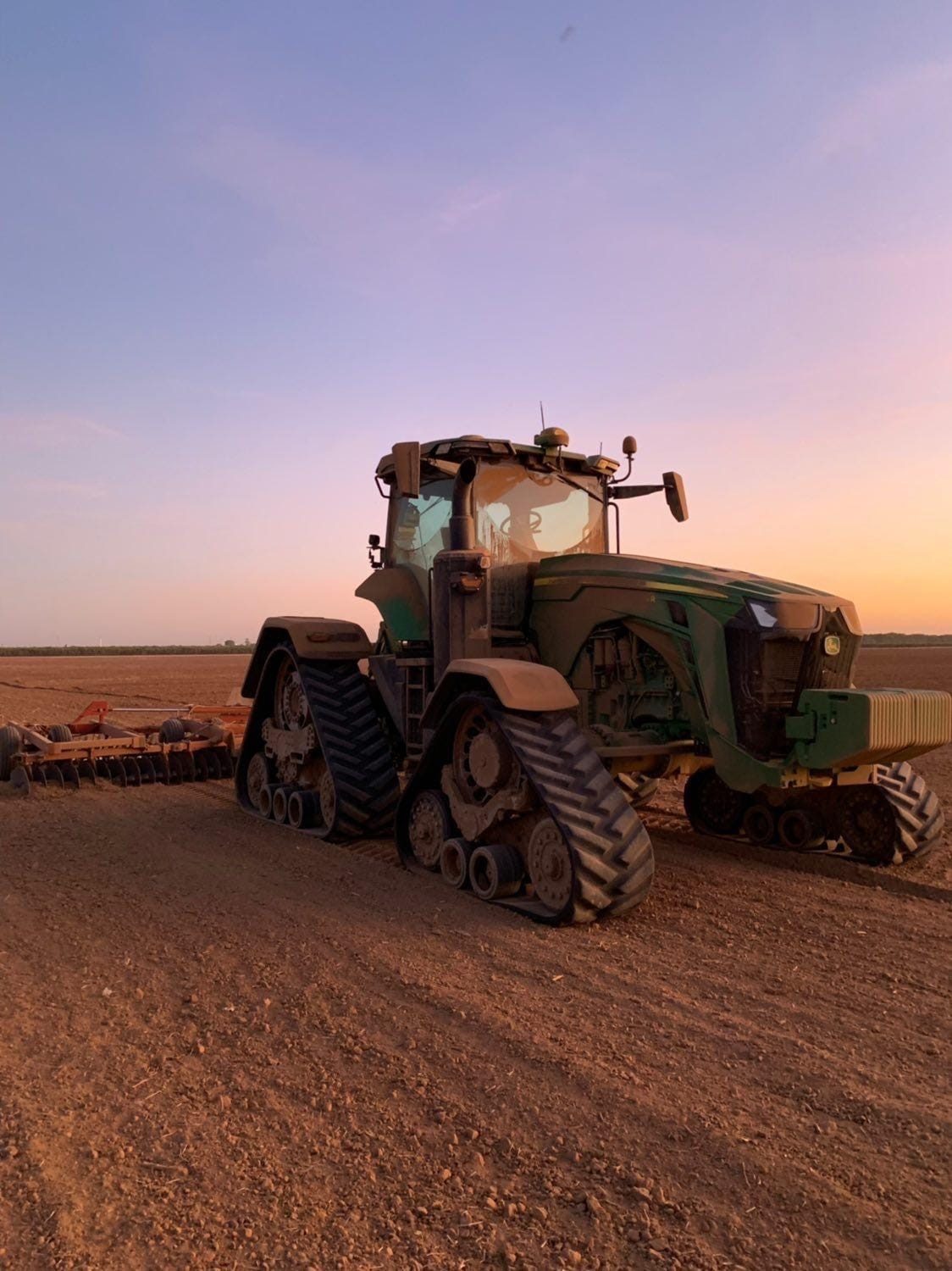 A four-track John Deere tractor against the evening sky.