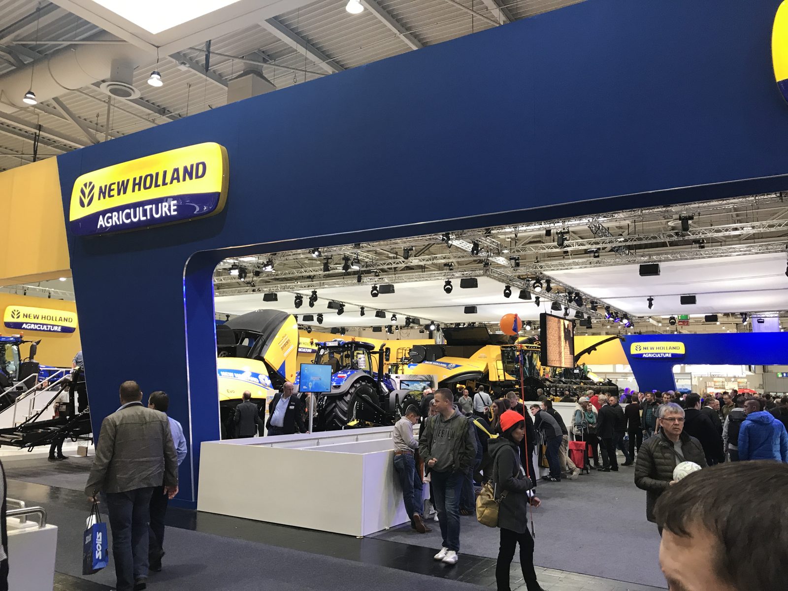 Tractors and harvesting equipment at a New Holland Agriculture trade-show booth.