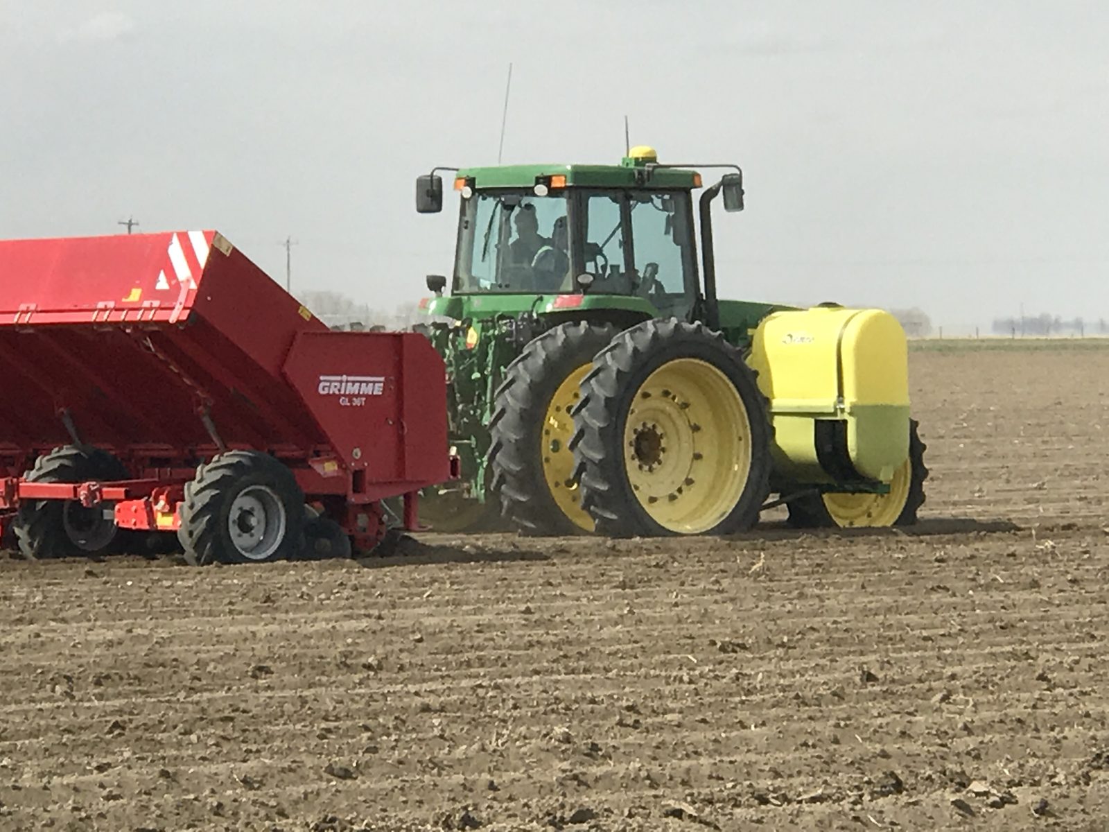 A John Deere tractor pulling a red GRIMME potato planter.