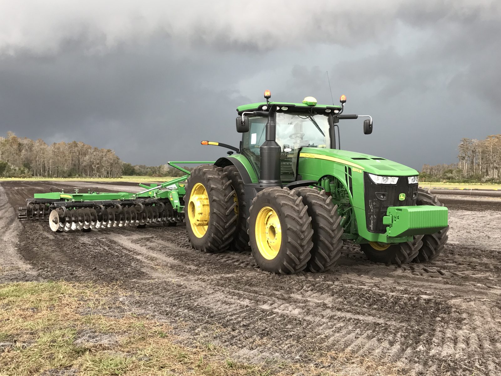 An 8370R with dual wheels and a disc implement beneath storm clouds.
