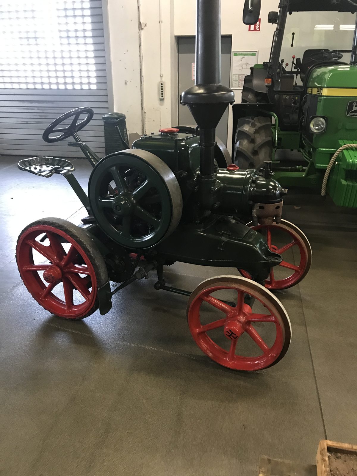An early tractor with an exposed flywheel and red spoked wheels.