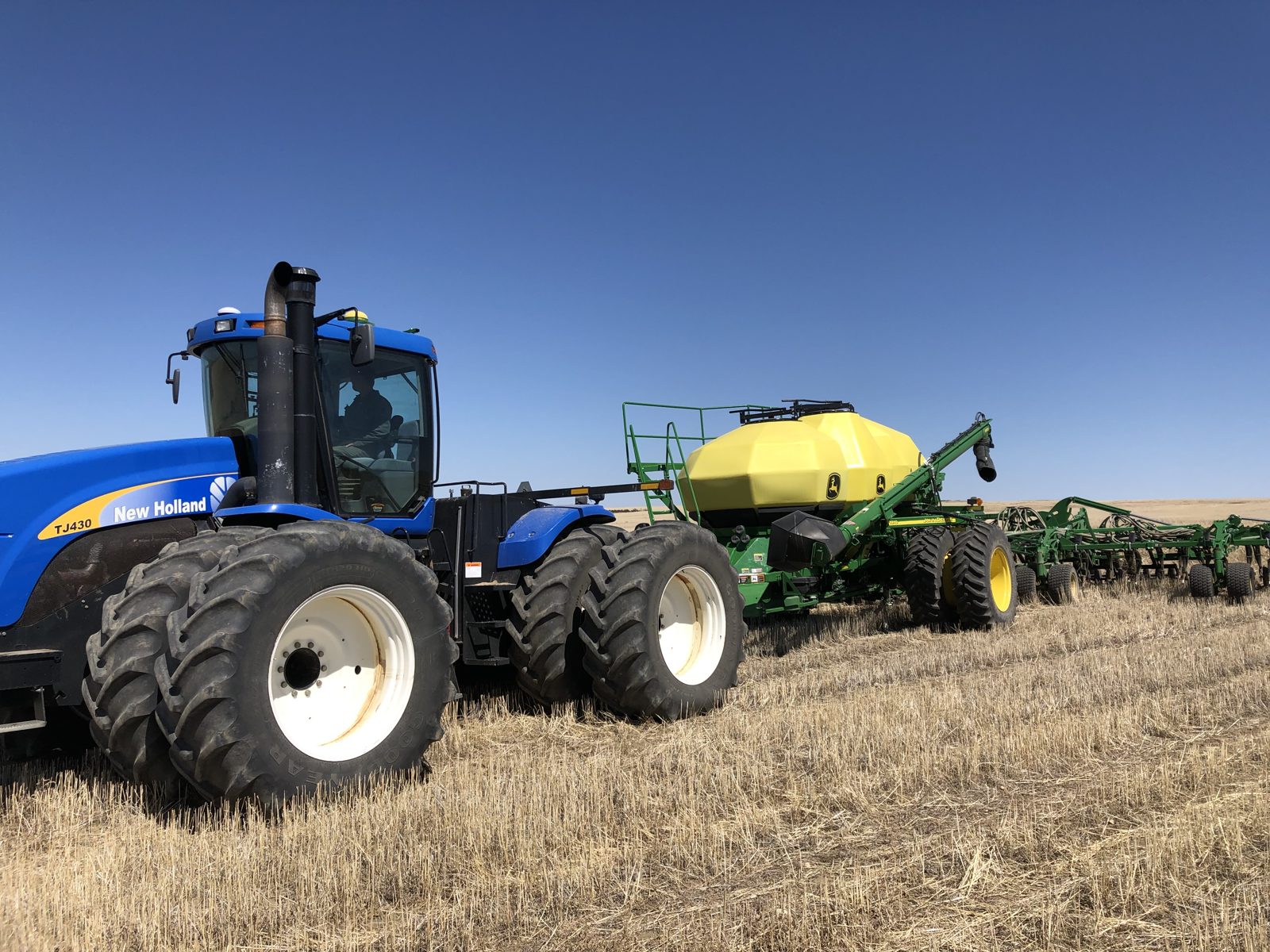 A New Holland TJ430 tractor paired with John Deere air-seeding equipment.