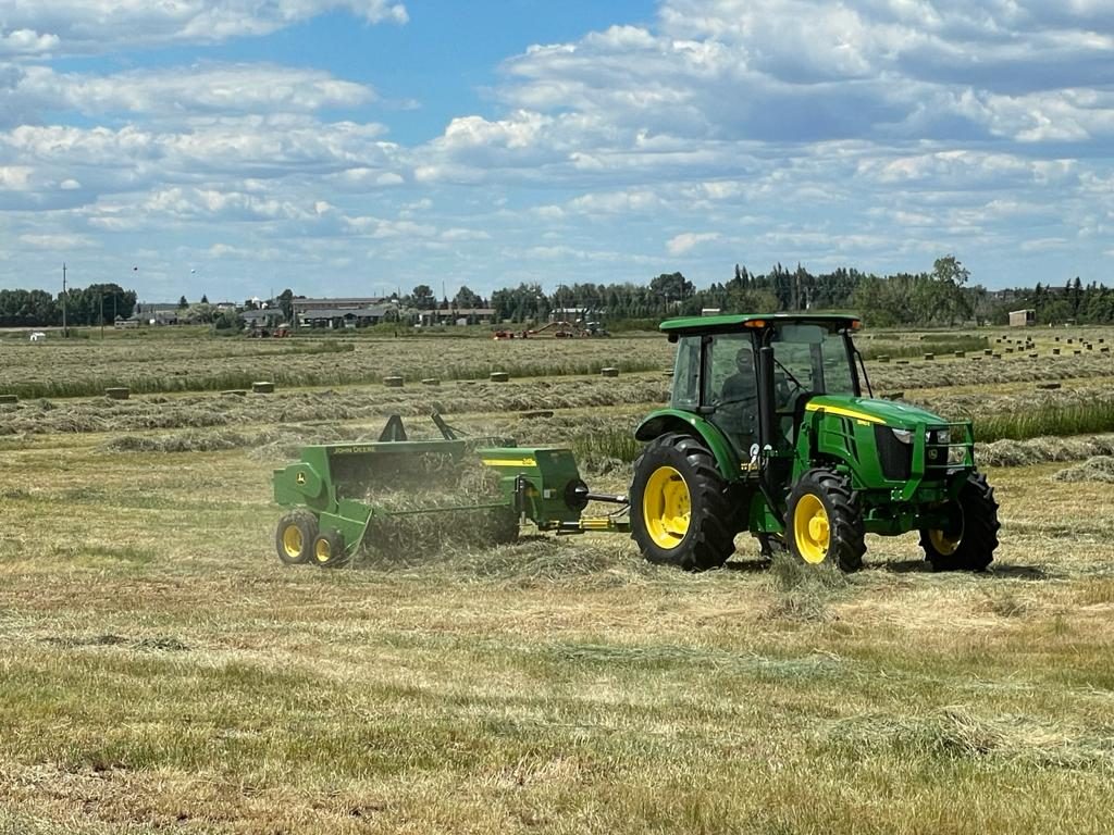 A John Deere tractor and baler working through a hay field.