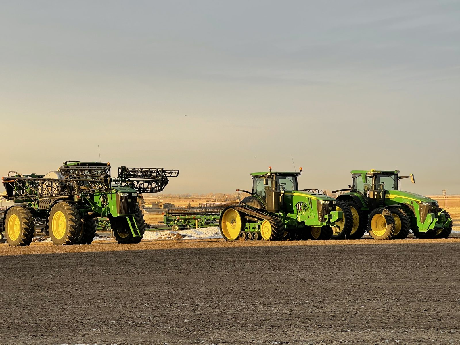 A sprayer, tracked tractor, and wheeled tractor together in the field.