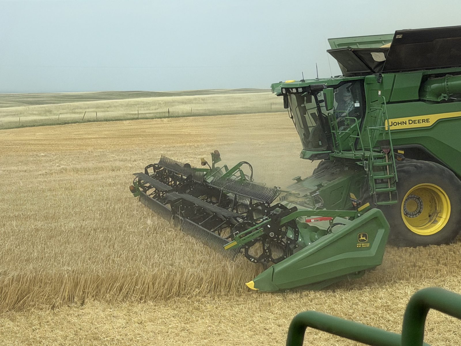 A John Deere combine works through standing grain with a wide header.