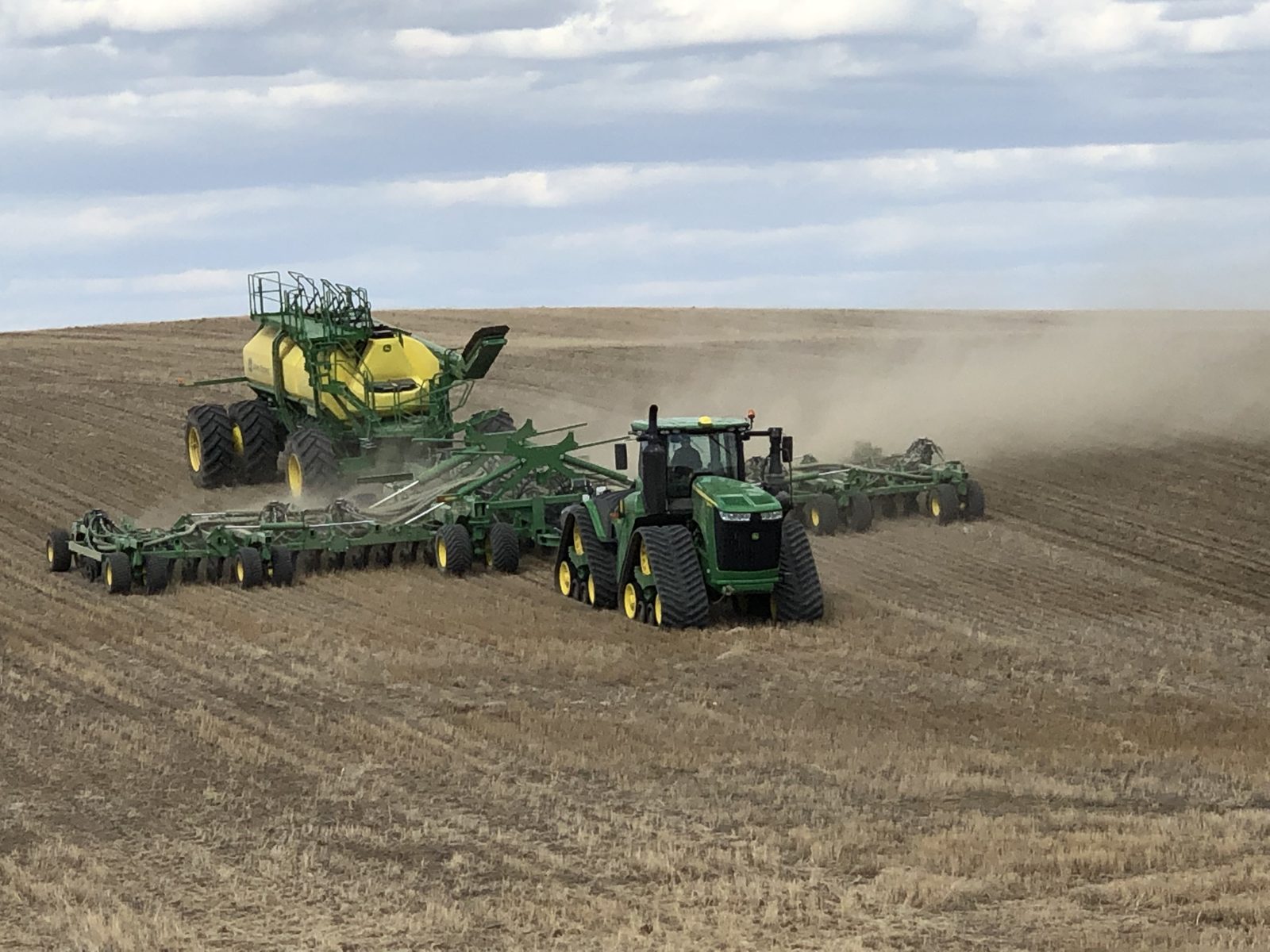 A tracked John Deere tractor pulling an air drill and cart.
