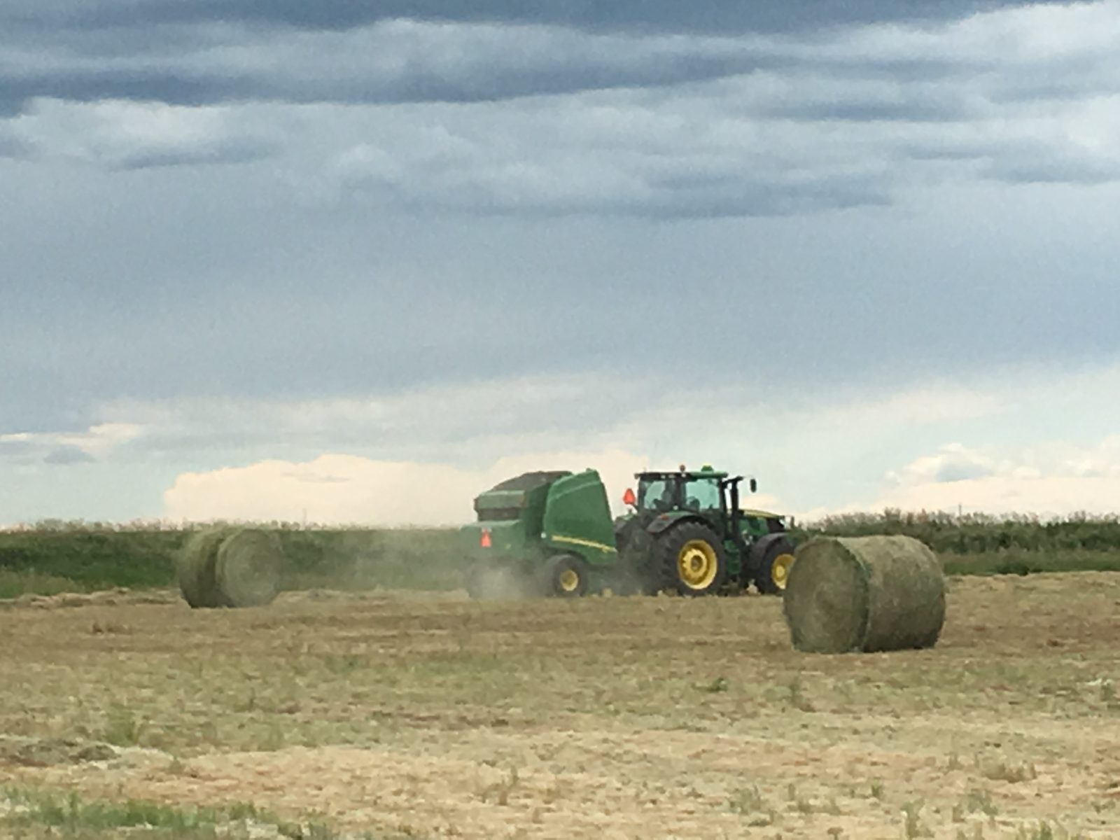 A John Deere tractor and round baler among freshly made hay bales.