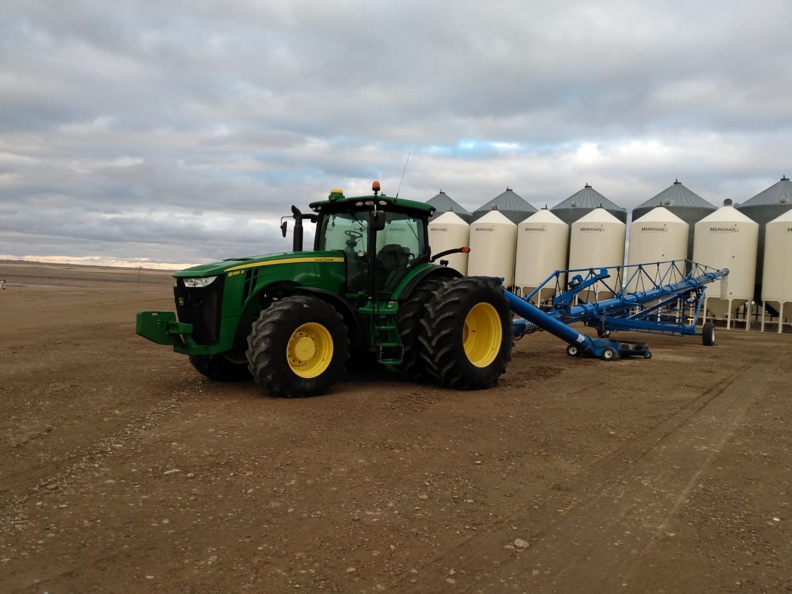 A John Deere tractor beside grain storage bins and an auger.