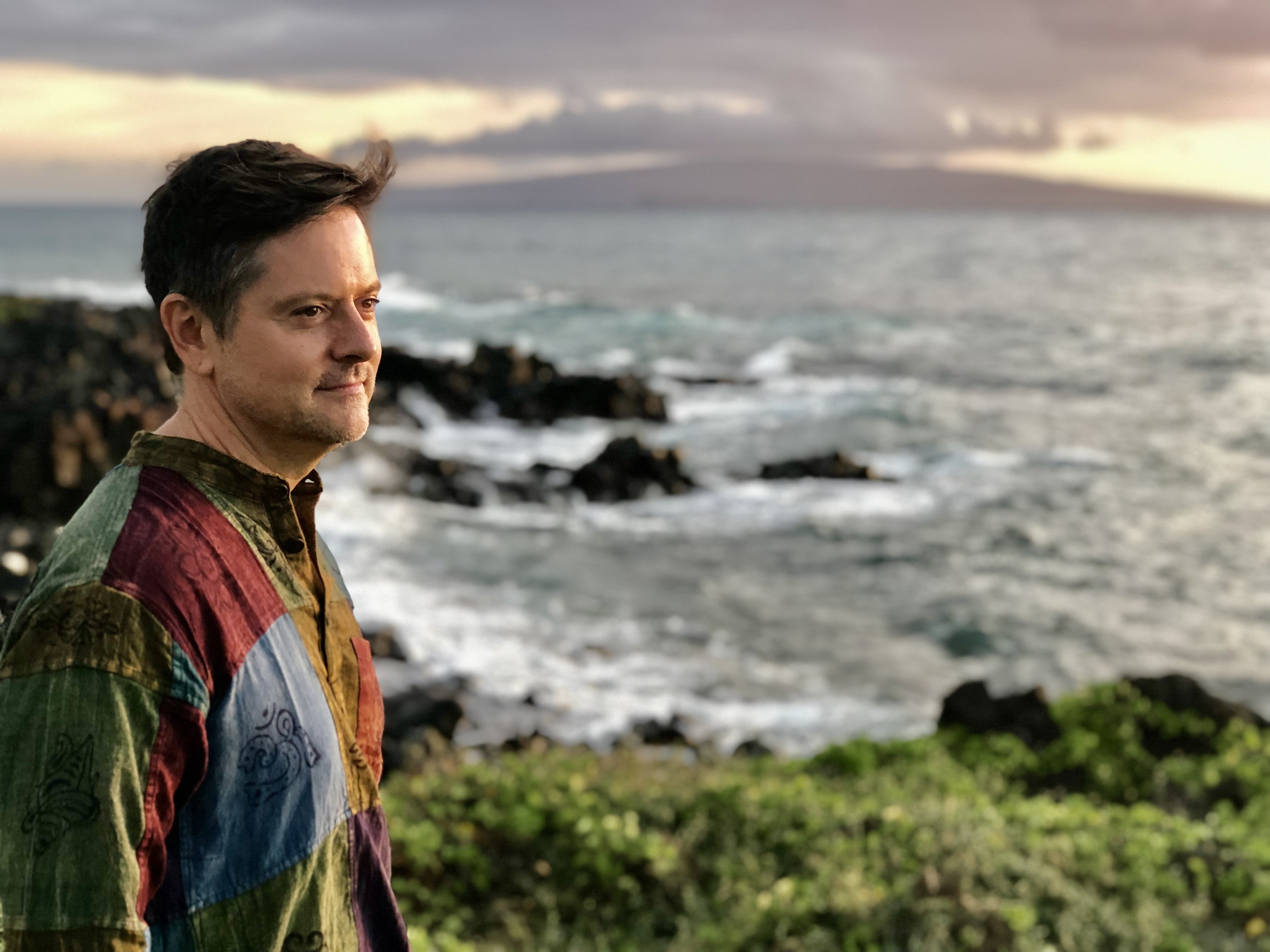 Paul Denniston standing on a rocky coastline at sunset