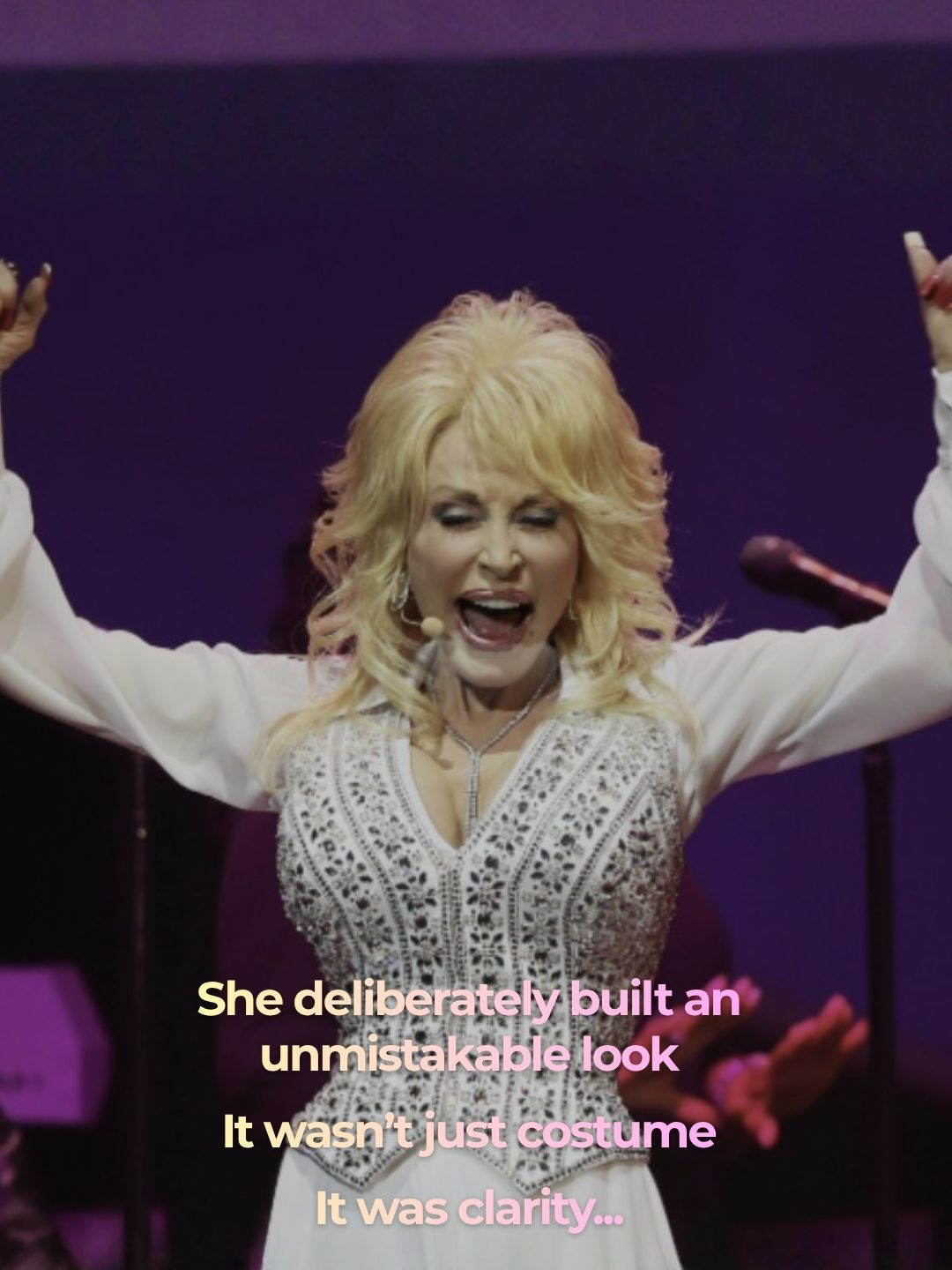 Dolly Parton performing with arms raised in a white beaded outfit &mdash; 'She deliberately built an unmistakable look. It wasn't just costume. It was clarity.'