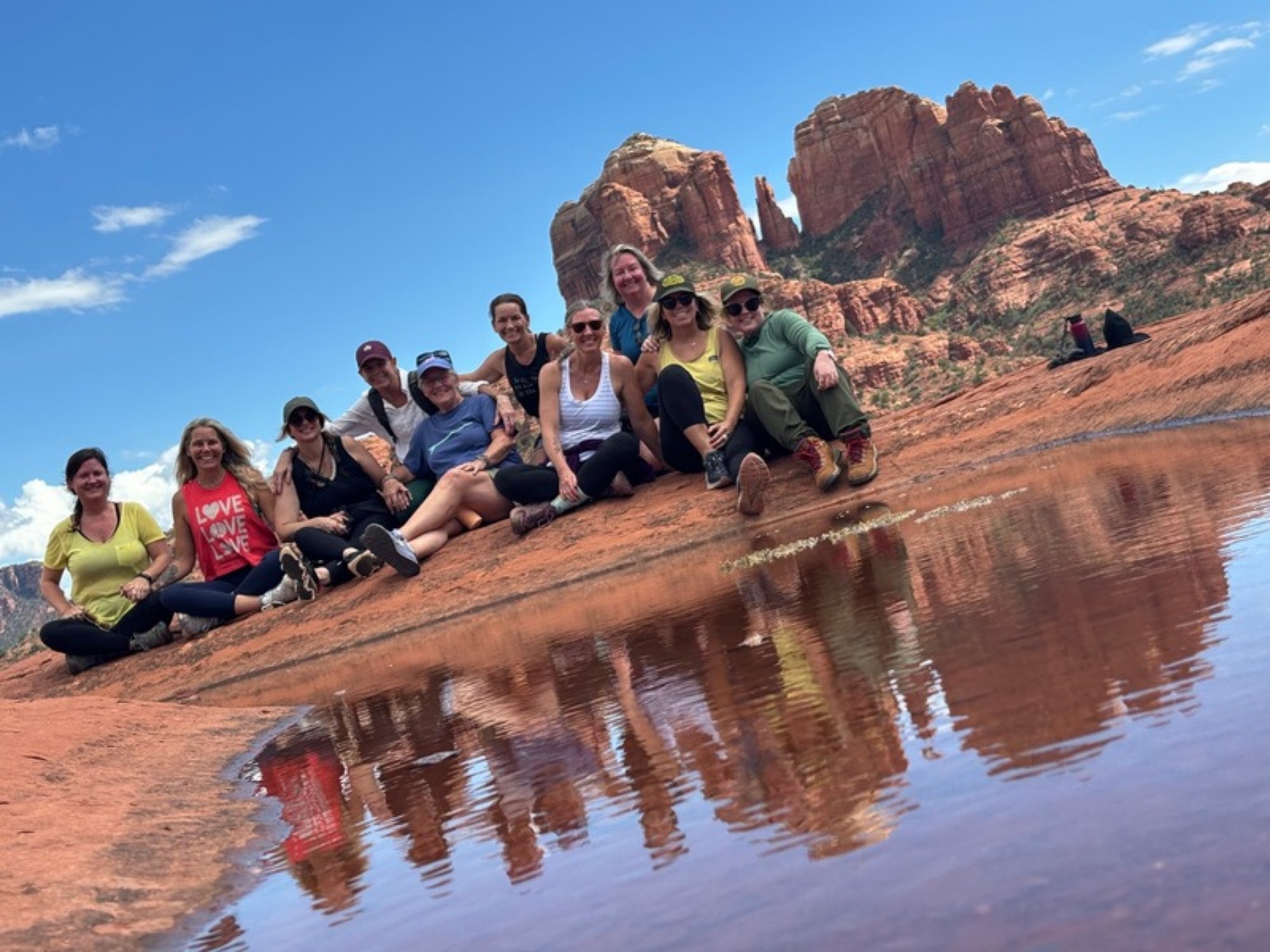 A group of women seated on red rock, reflected in water below Cathedral Rock