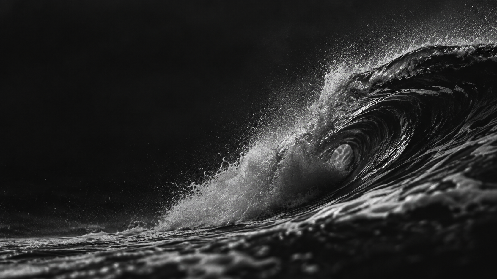 A dark ocean wave folding into silver spray.