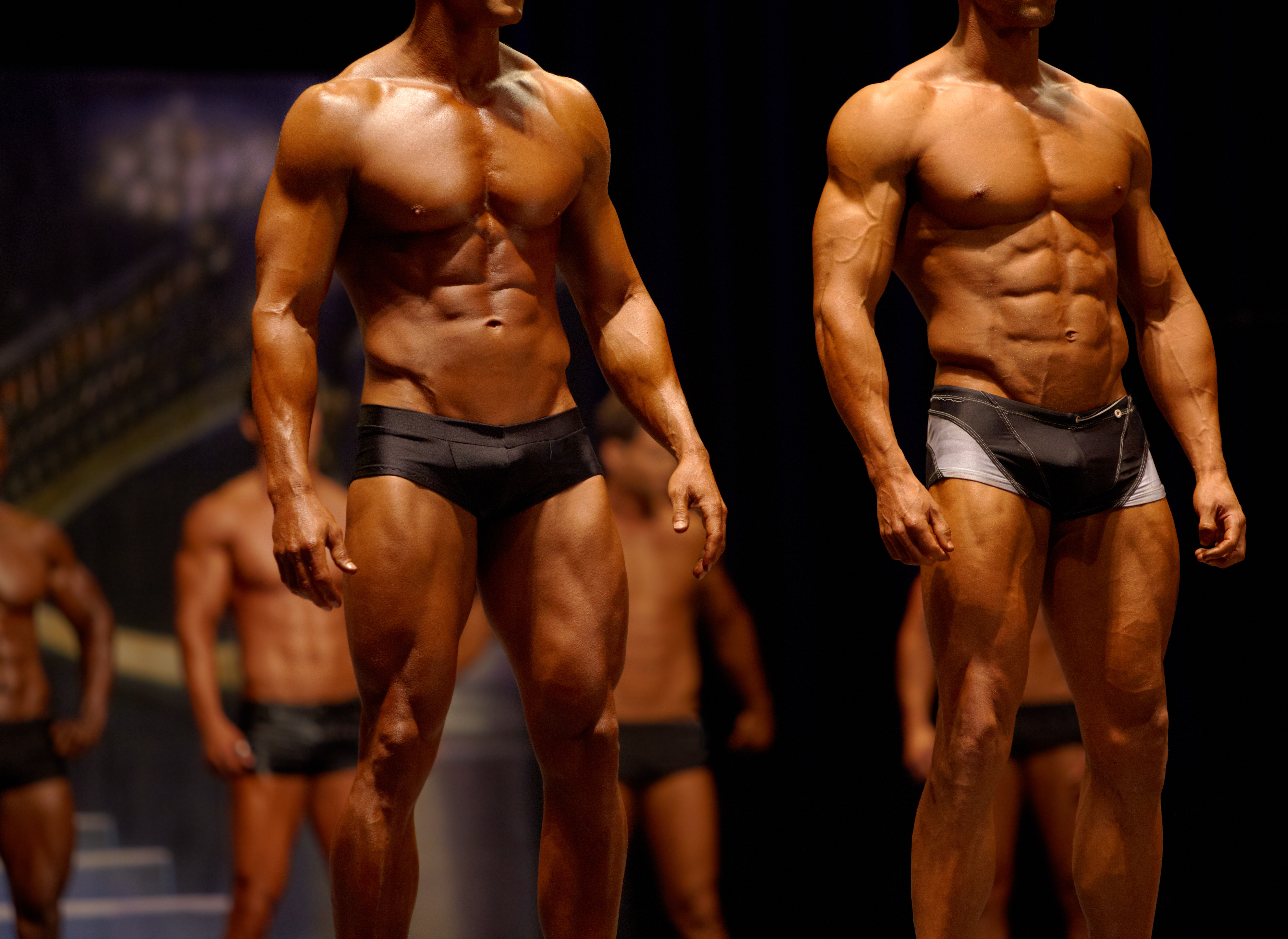 Physique athletes standing in a stage comparison lineup