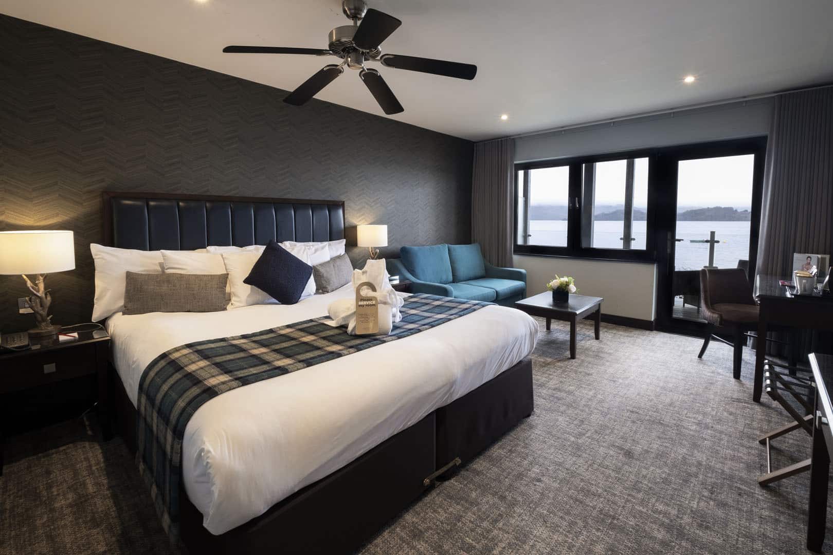 A lodge bedroom with tartan bed runner and doors opening to the loch