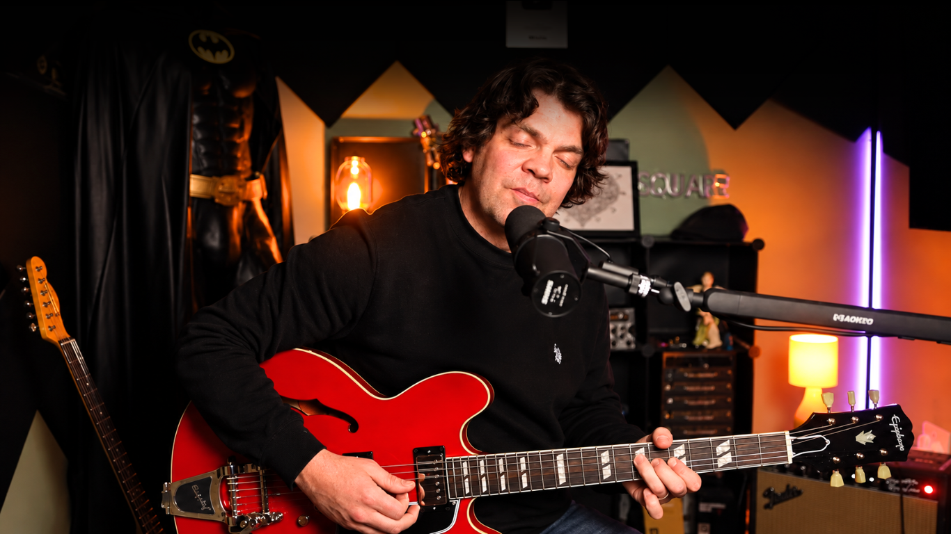 Tony playing a red hollow-body electric guitar with his eyes closed