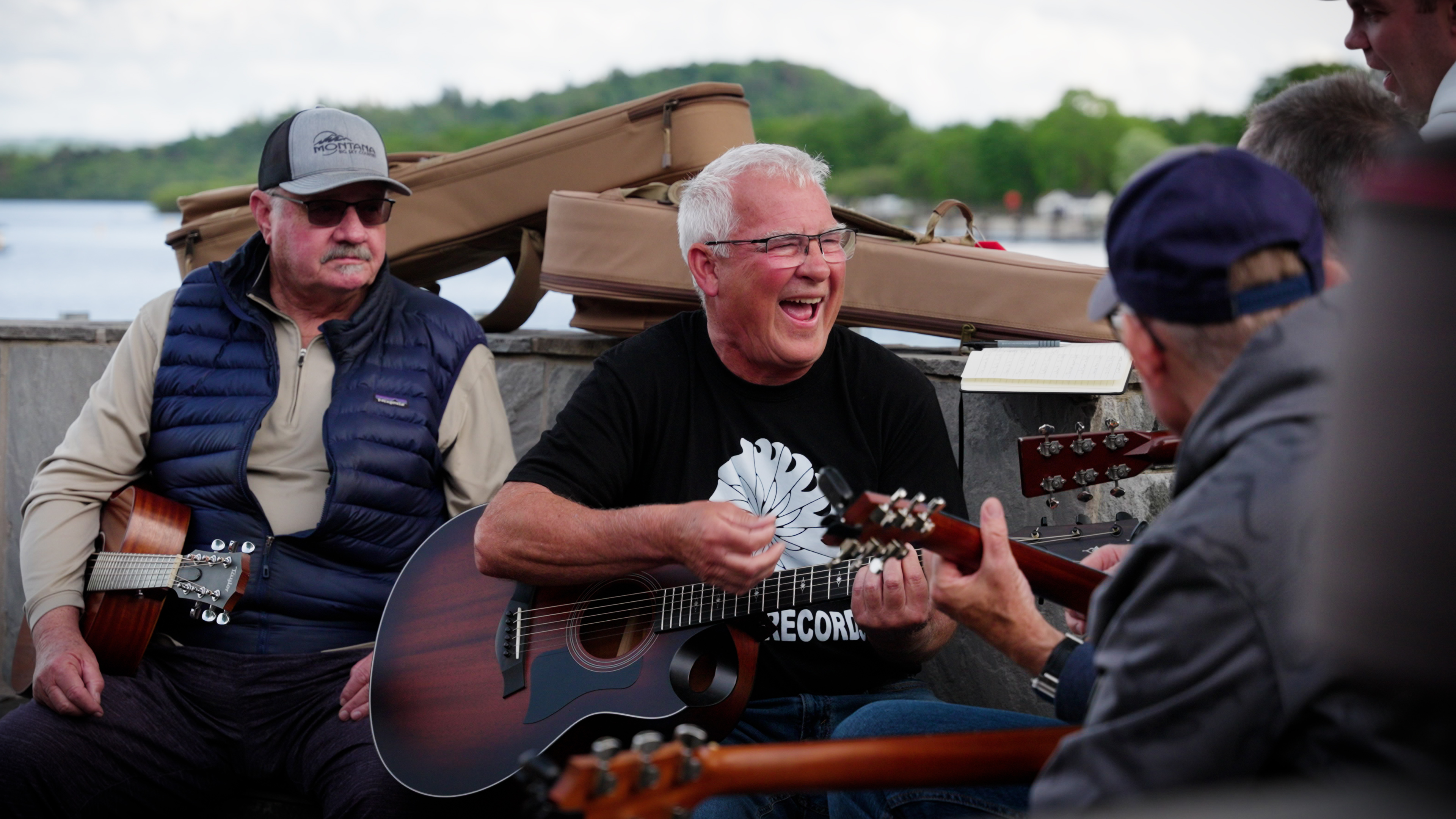 A guitarist laughing mid-song beside the loch