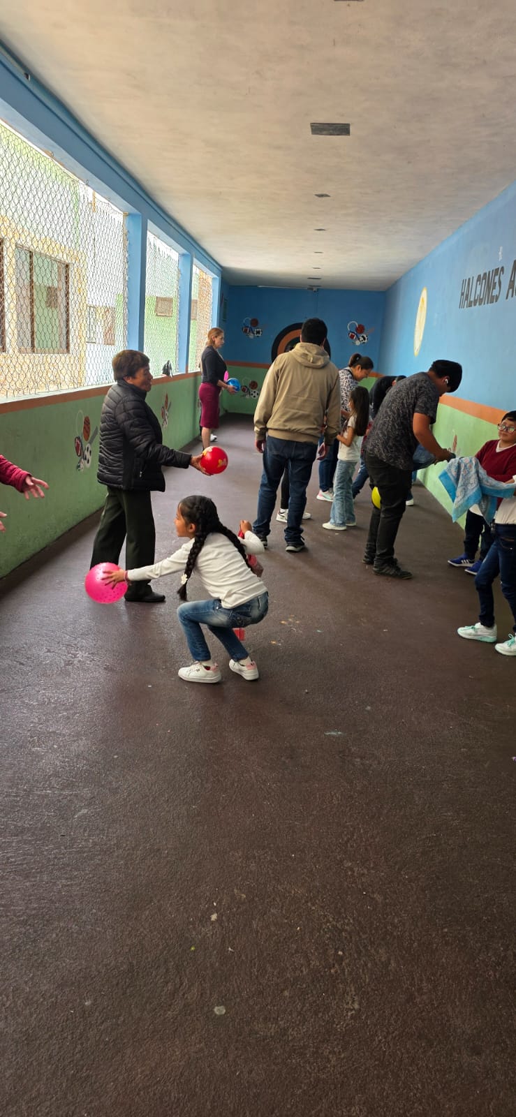 Estudiantes y familias participando en una dinámica con pelotas en el salón de usos múltiples