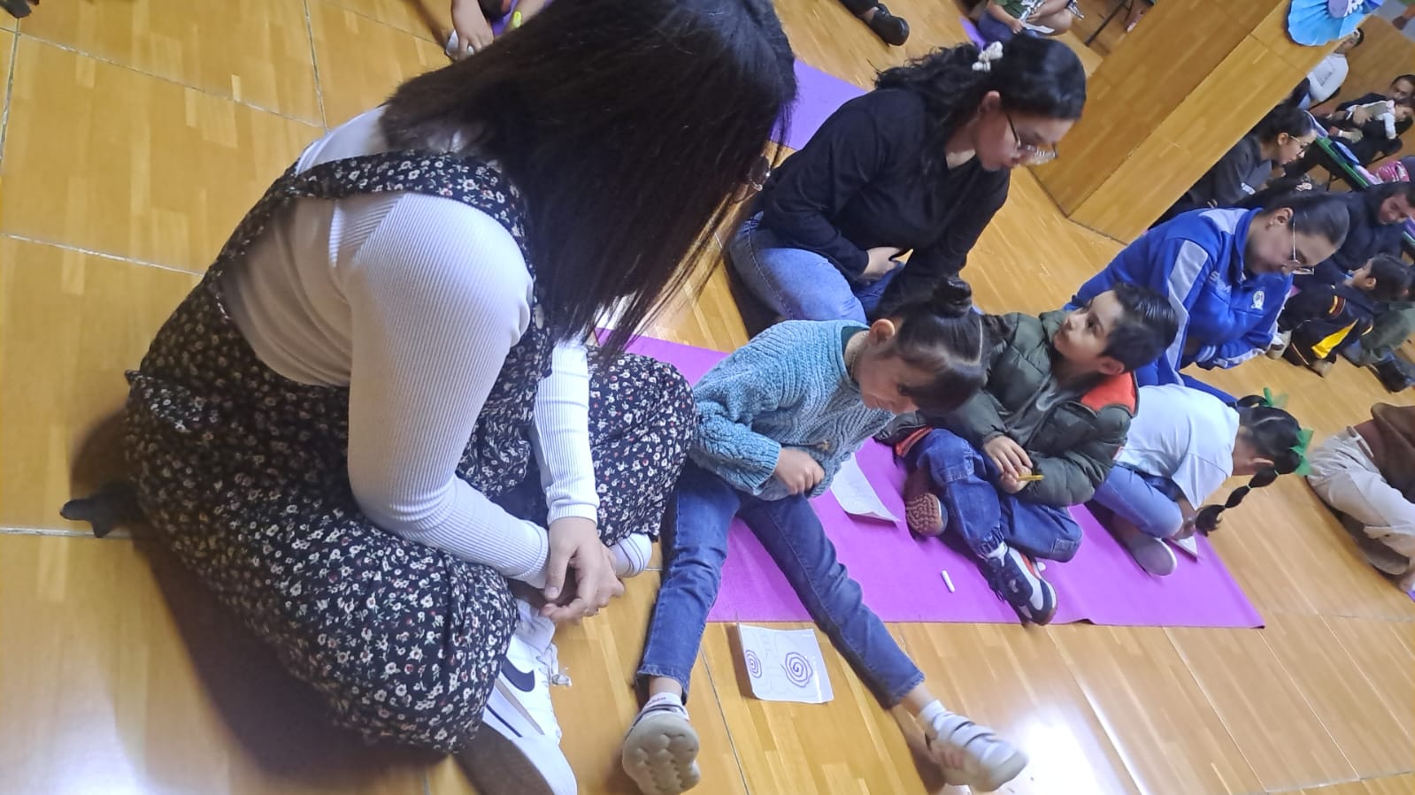 Madres e hijos realizando una actividad sentados en tapetes morados