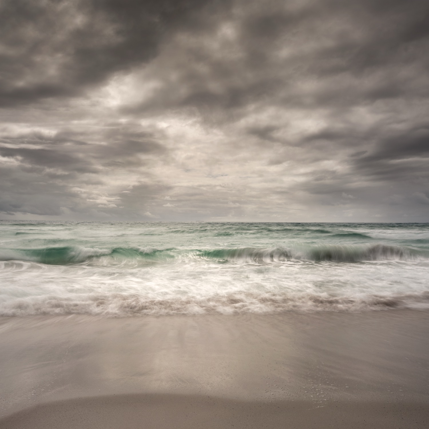 Heavy cloud building over a green sea with surf running in below