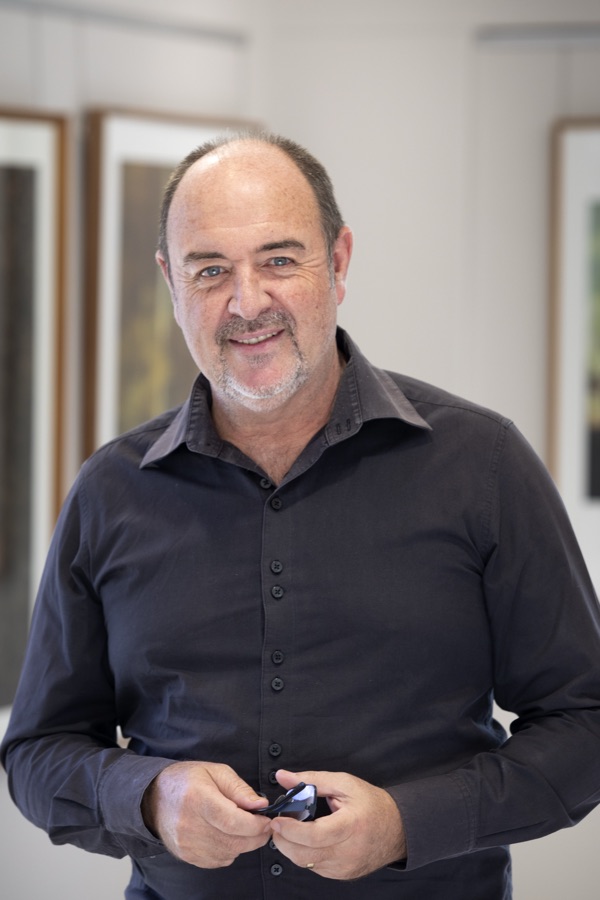 Martin Osner standing in his gallery with framed artworks behind him