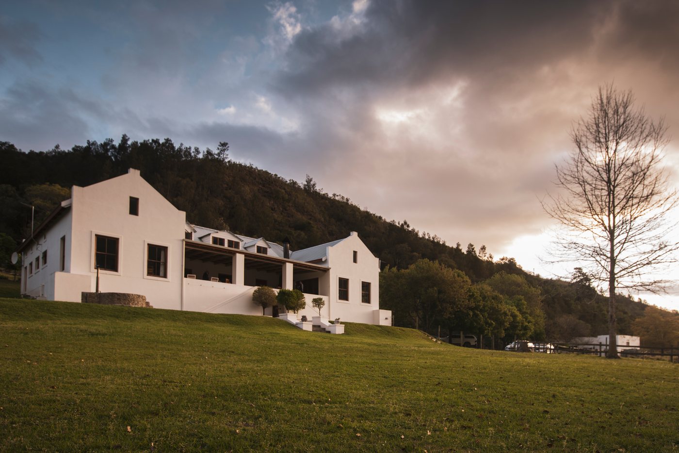 A white gabled manor house beneath the mountain under a dramatic sky