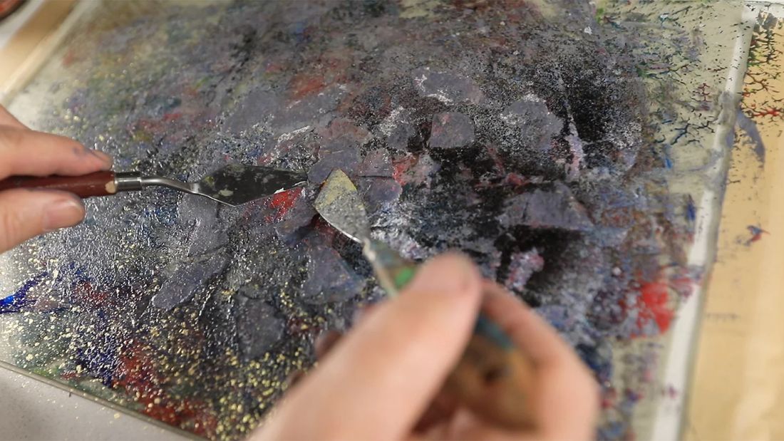 A palette knife pressing paint into a glass fused surface