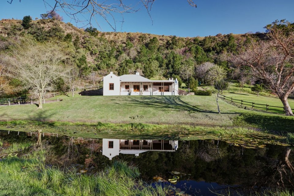 A whitewashed cottage reflected in still water with the hills behind