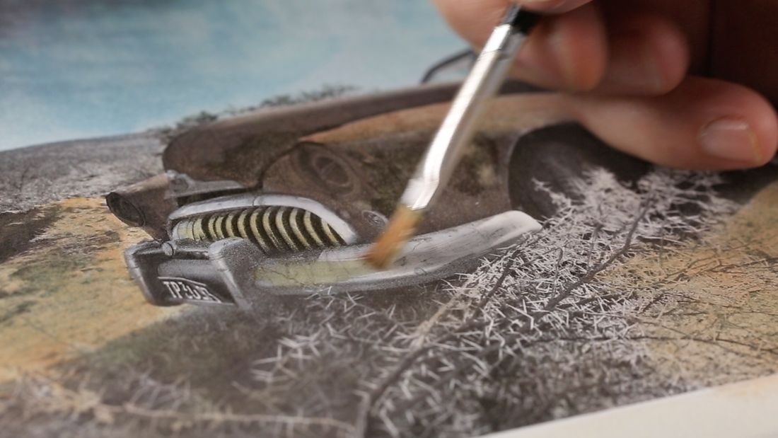 A fine brush adding paint by hand to a printed photograph