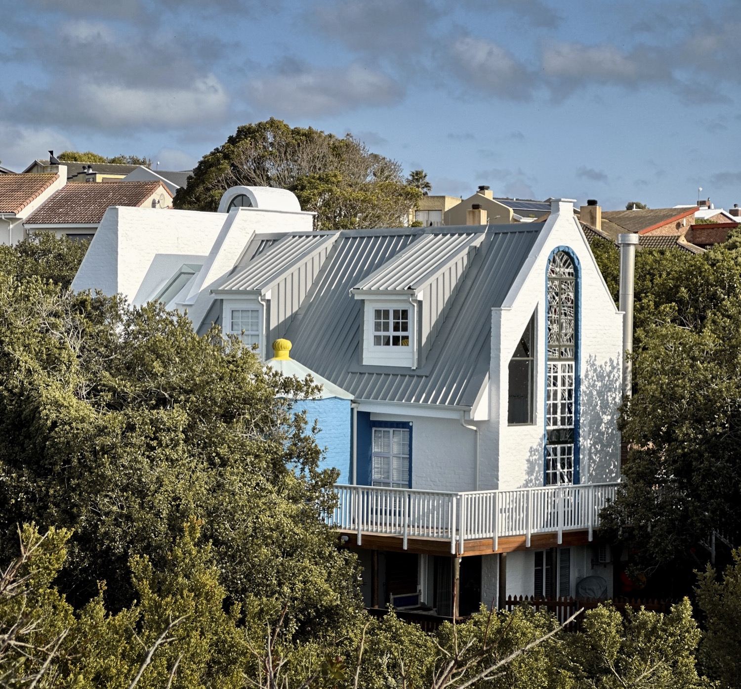 White gabled house with a blue front and a wide deck, set in milkwood trees