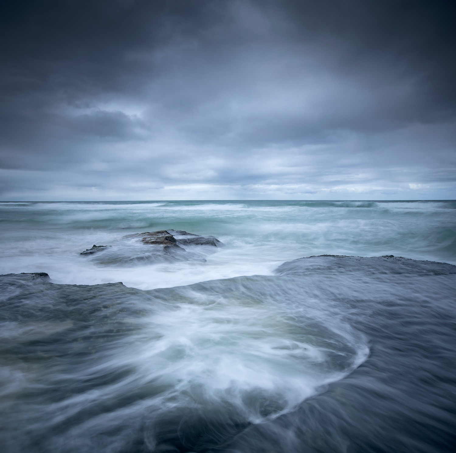 Blue long exposure of the sea washing over a low rock shelf at dusk