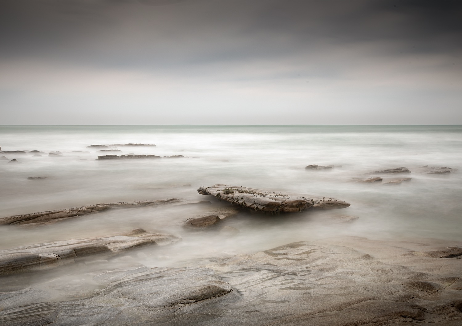 Pale long exposure of the sea drawing back off a flat rock shelf