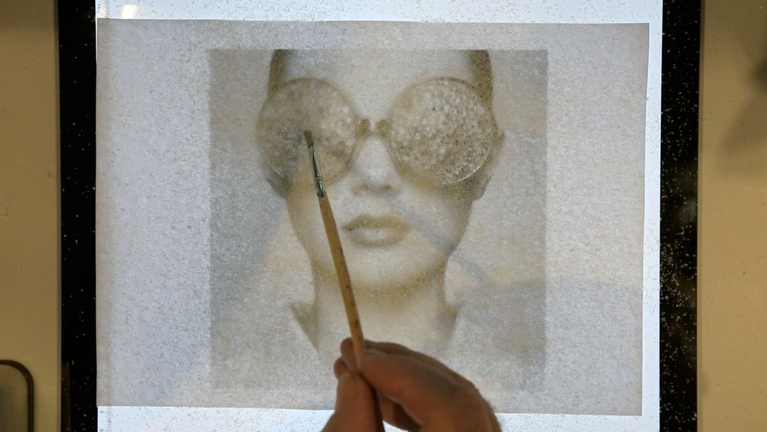 A brush laying crystal medium over a portrait
