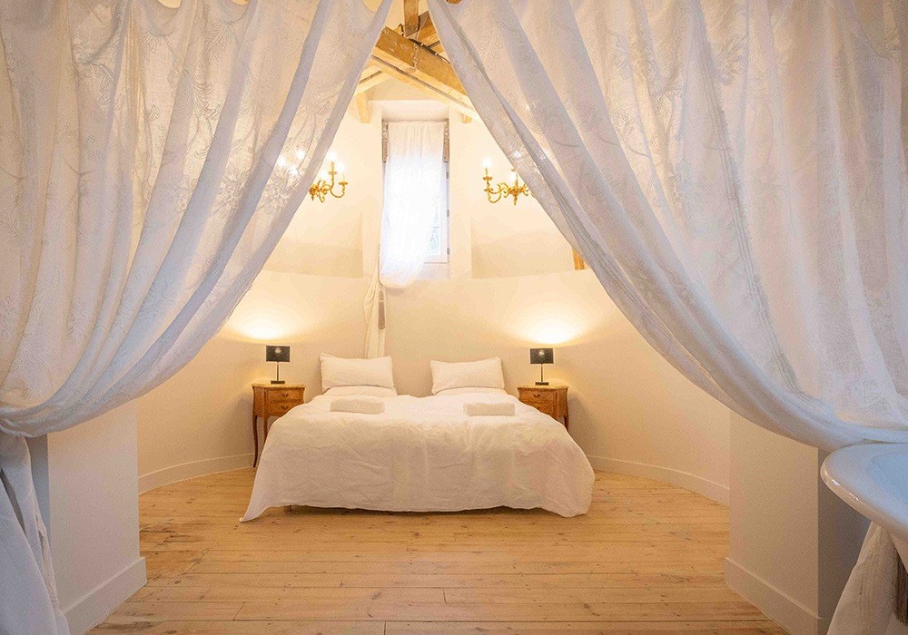 Château bedroom with white drapes and a soft lit window