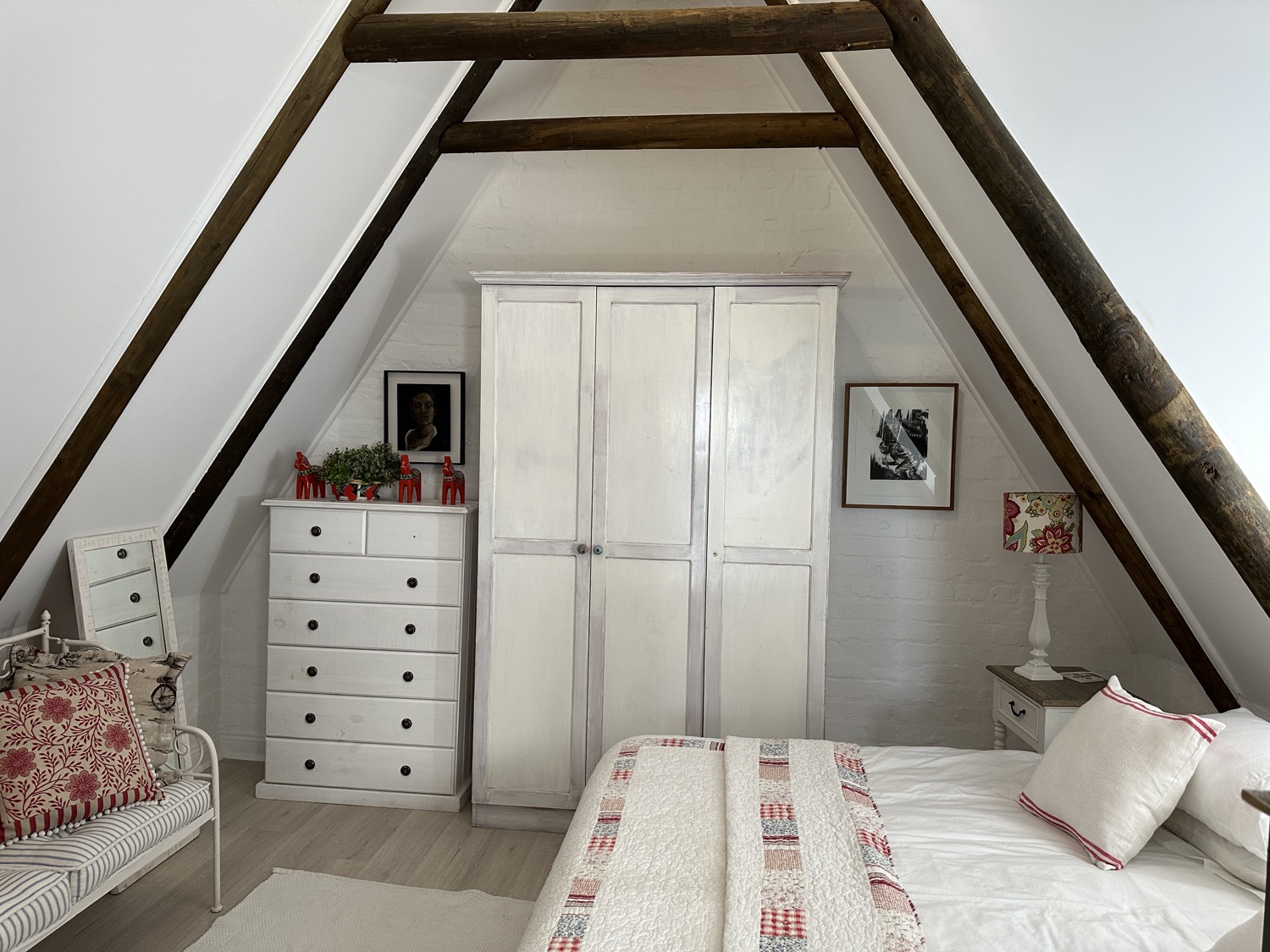 Attic guest room under exposed beams with a white cupboard and bed