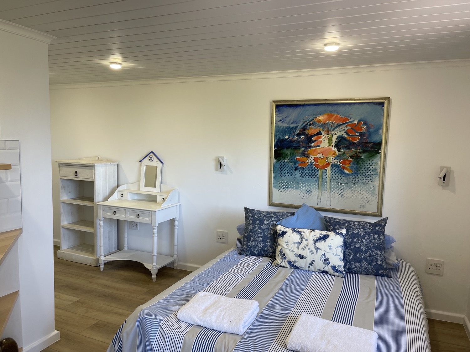 Guest bedroom in blue and white with a framed painting above the bed