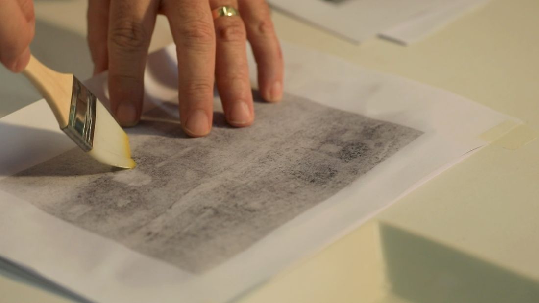 A flat blade sweeping black powder across a transfer sheet