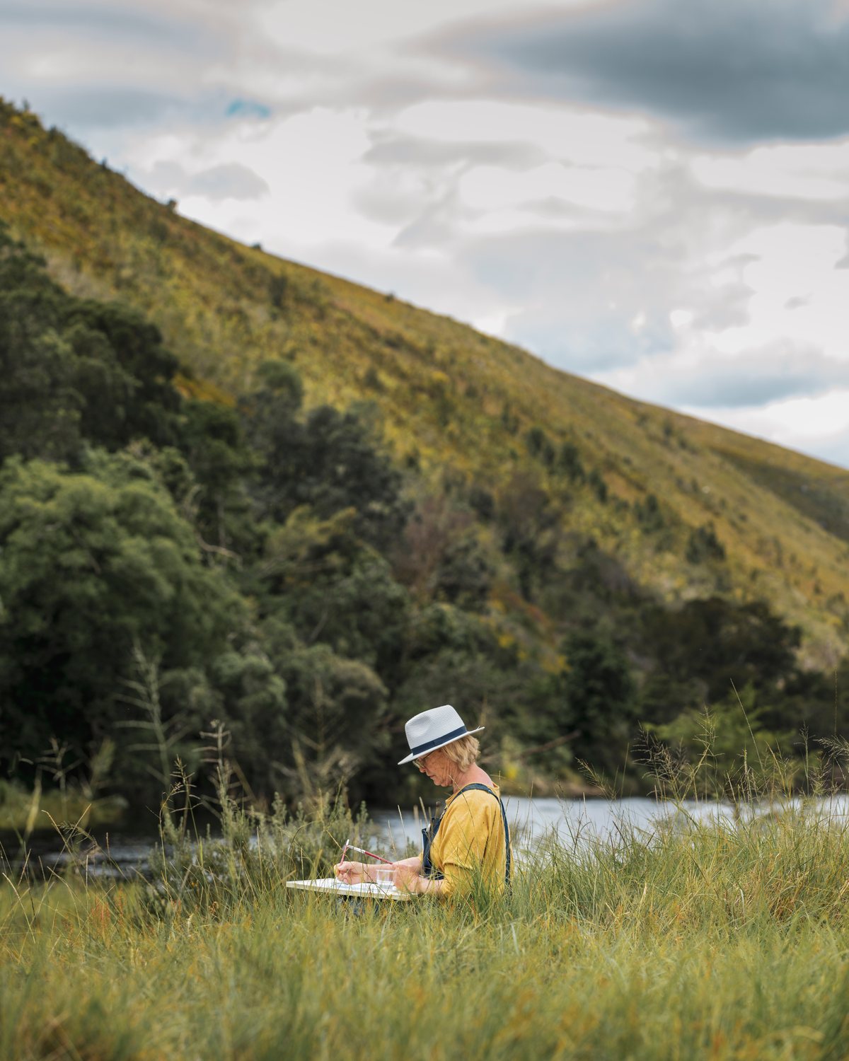 A student painting outdoors in the field with the hills behind
