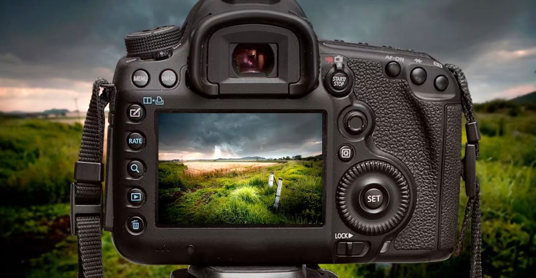 A camera on a tripod in the field, the landscape showing on the screen on the back