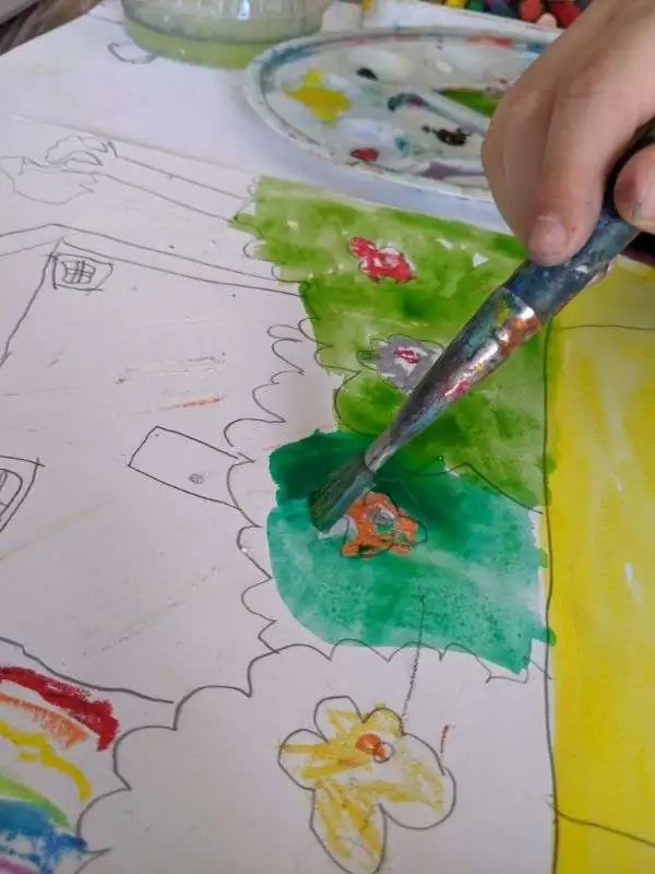 A child watercolour-painting a house scene