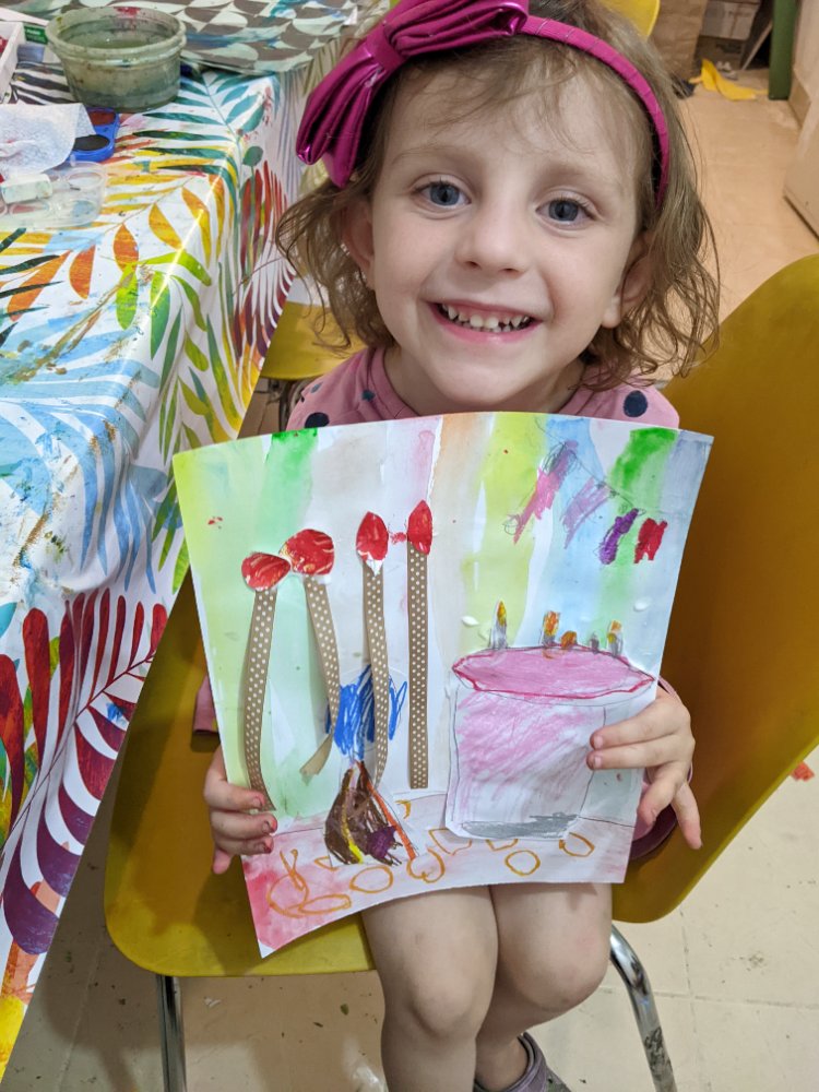 A young girl beaming as she holds up her painting